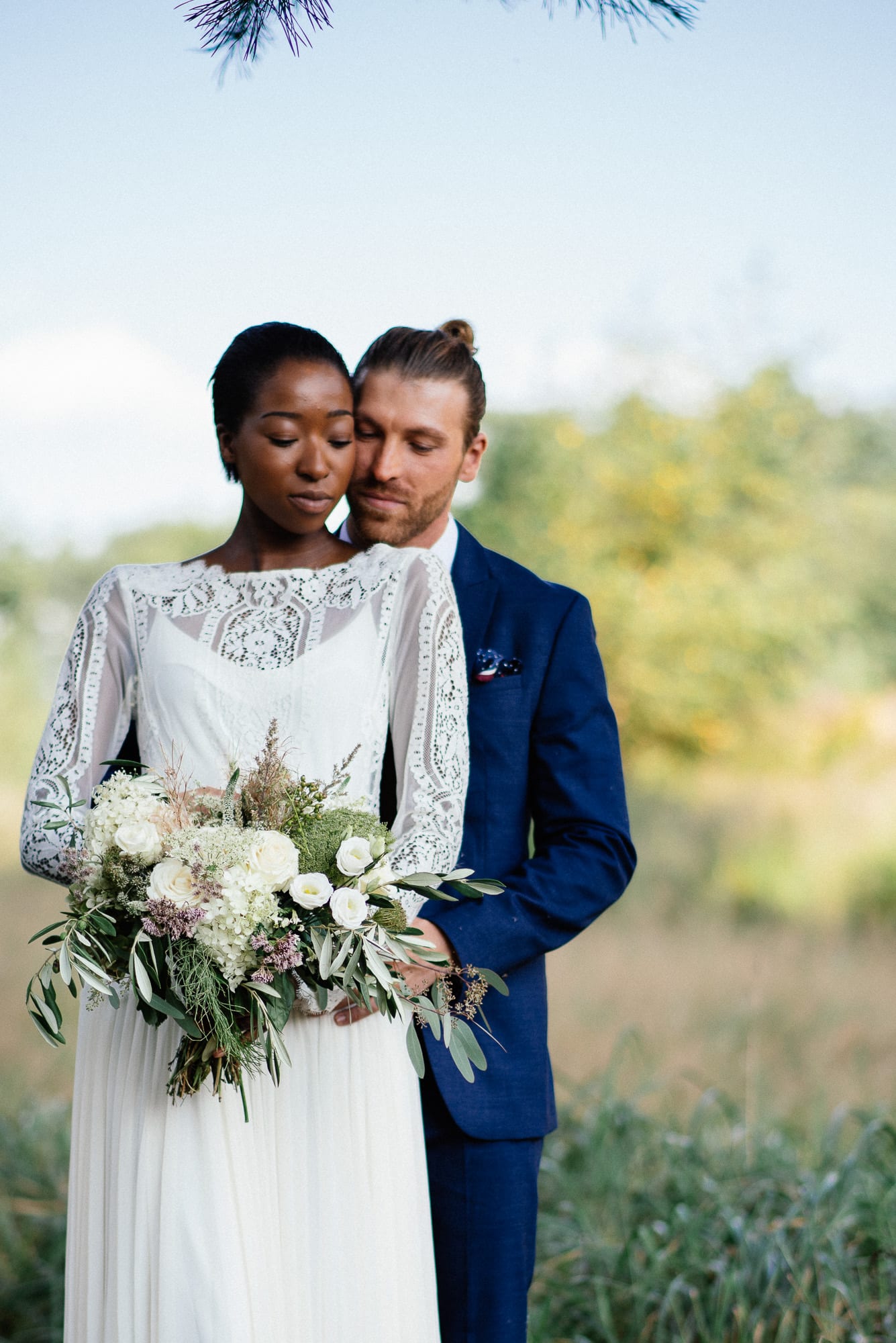 Eine Braut und ein Bräutigam umarmen sich draußen, während die Braut einen Blumenstrauß hält.