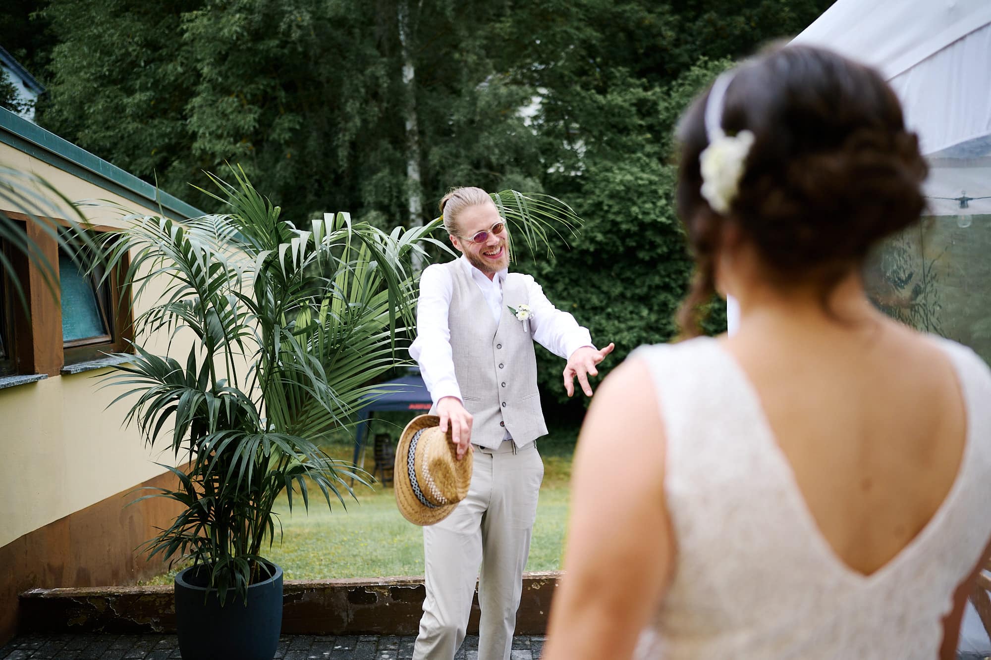 Der Bräutigam im weißen Anzug lächelt und deutet auf die Braut bei einer Hochzeit im Freien.