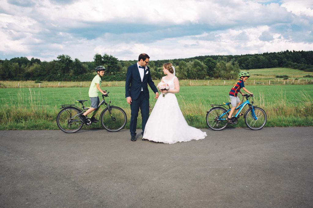 Radfahrende Kinder neben dem Brautpaar.