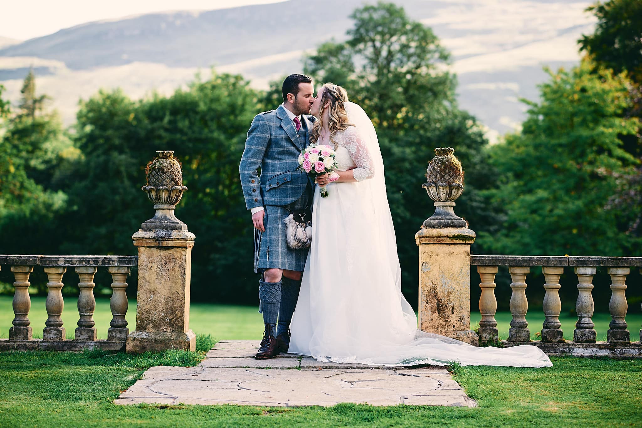 Ein frisch verheiratetes Paar küsst sich im Freien vor der malerischen Kulisse von Culcreuch Castle in Schottland.
