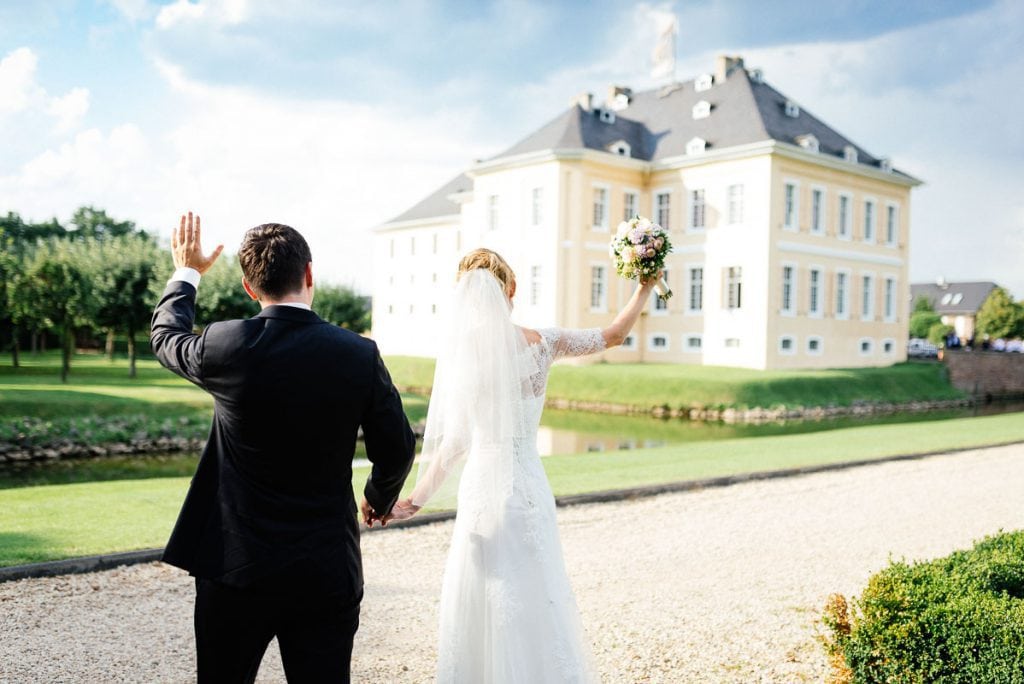 Das Brautpaar winkt den Gästen Am Schloss Miel.