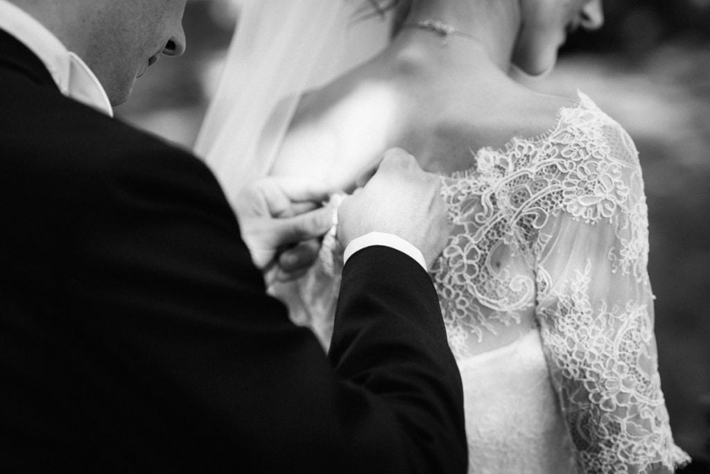 Der Bräutigam schließt das Kleid der Braut.