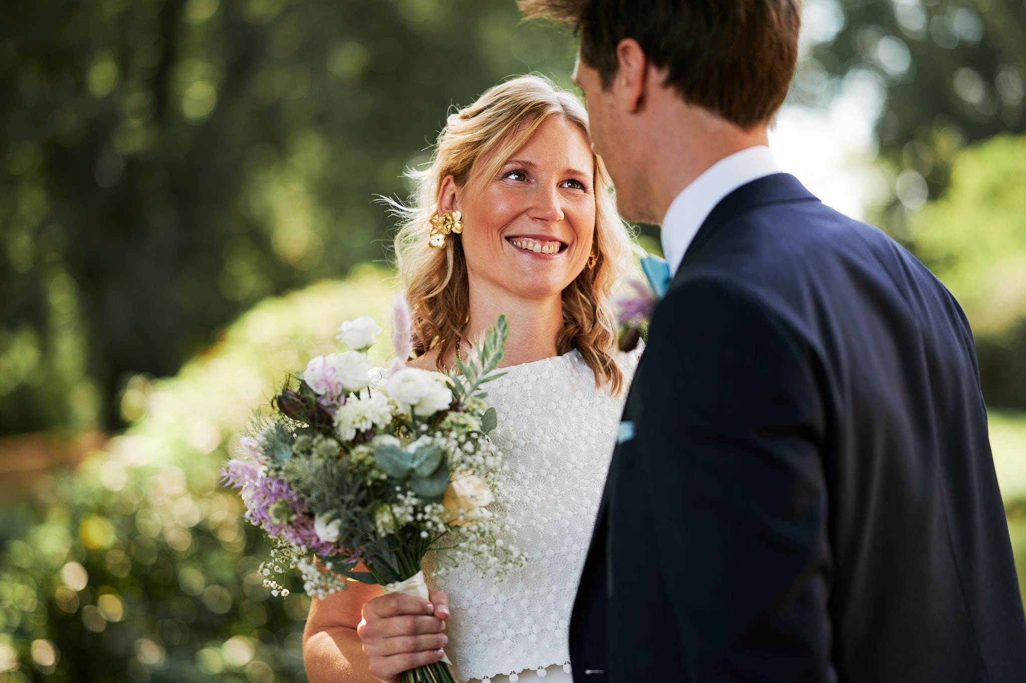 Die Braut lächelt den Bräutigam an, während sie während ihrer Herbsthochzeit einen Blumenstrauß im Freien hält.
