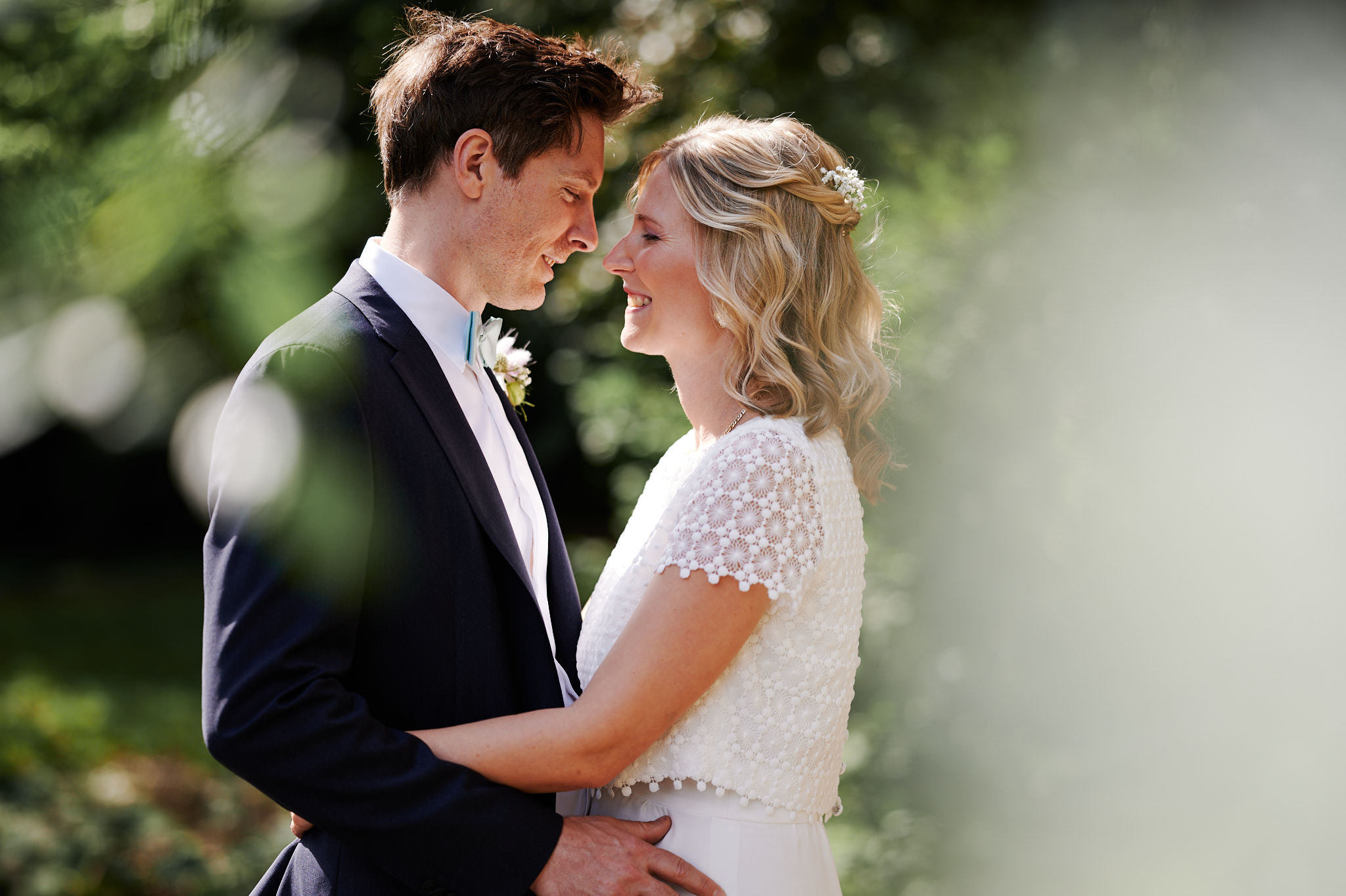 Eine Braut und ein Bräutigam verbringen einen zärtlichen Moment im Freien auf Schloss Wissen und blicken einander in die Augen, umgeben von viel Grün.