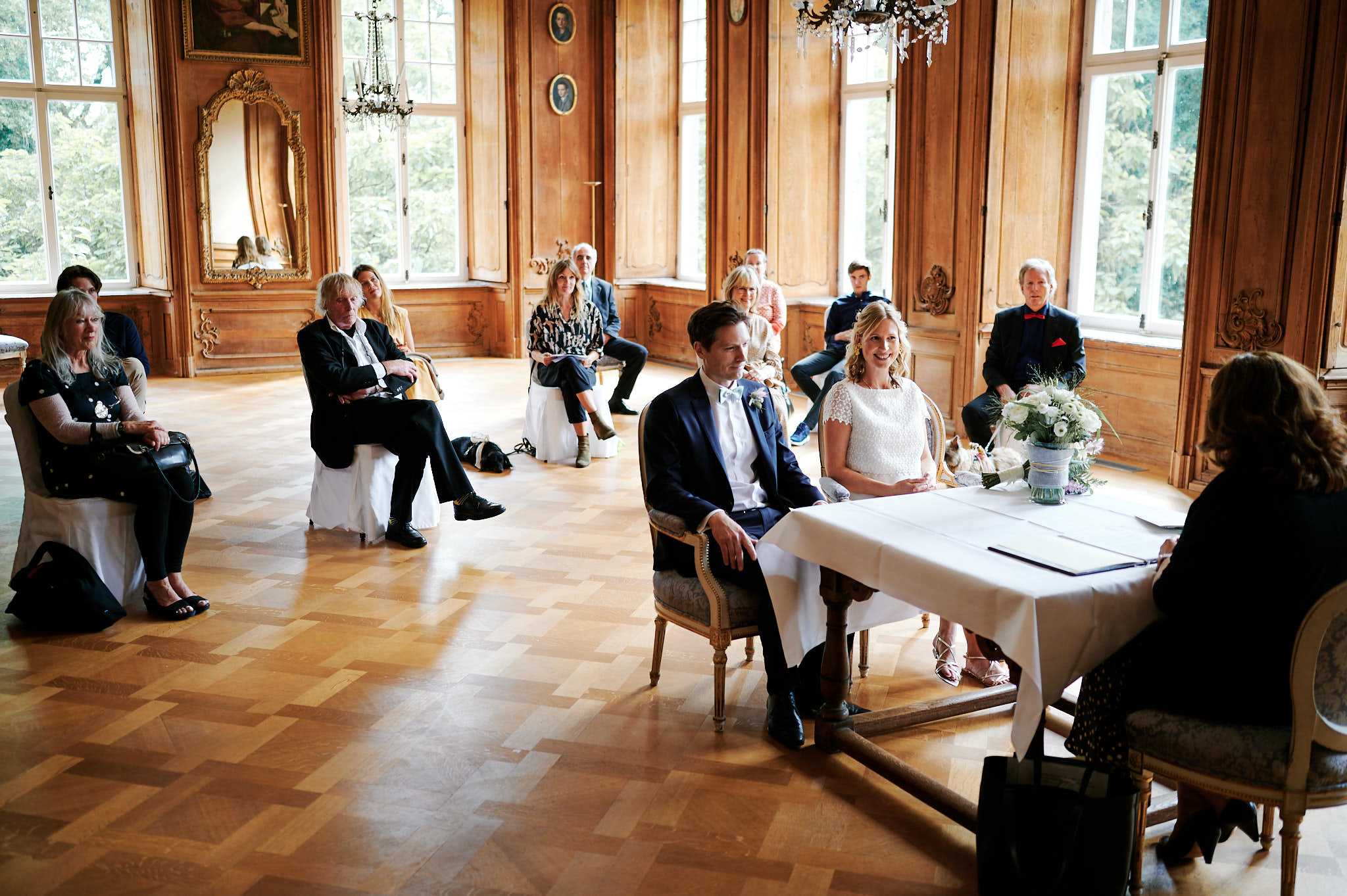 Ein Paar sitzt an einem Tisch während einer standesamtlichen Trauung in einem eleganten Raum im Schloss Wissen, während die Gäste zuschauen.