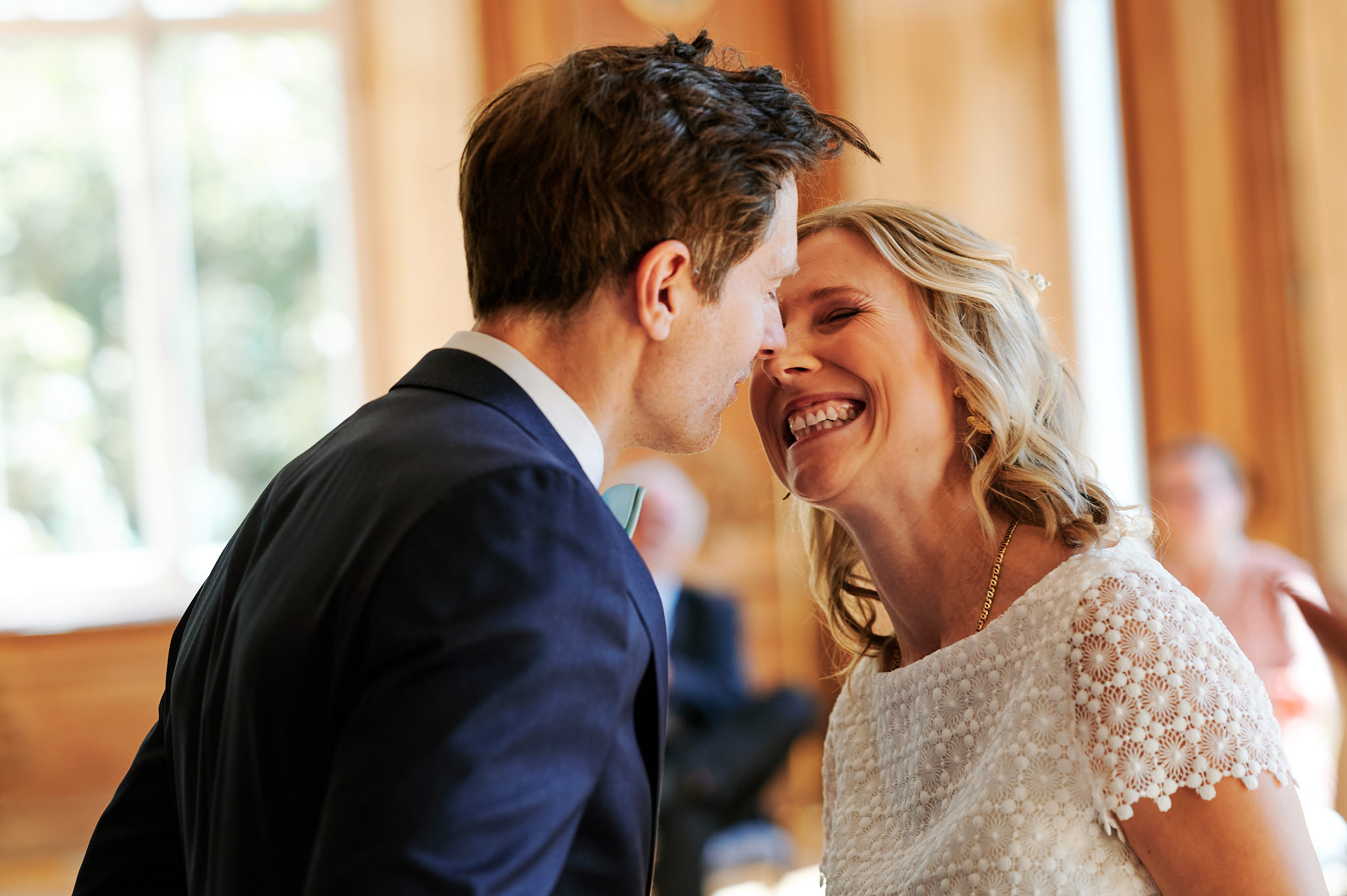 Ein glückliches Paar in formeller Kleidung teilt einen freudigen Moment bei seiner Hochzeit auf Schloss, wobei die Frau lacht und der Mann lächelt, während sie sich eng aneinander lehnen.