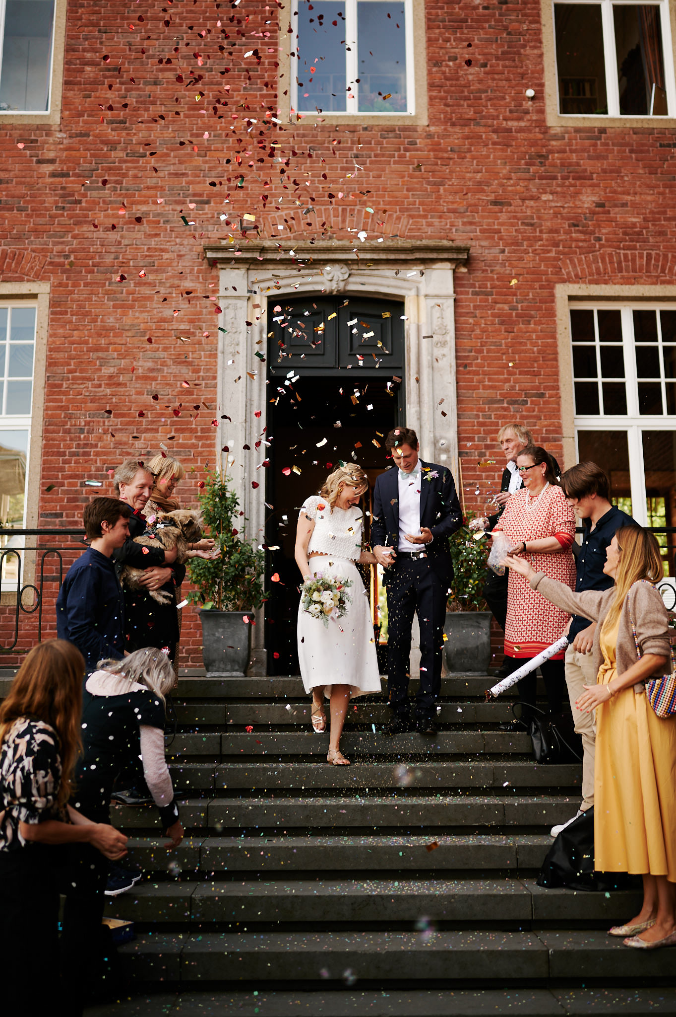 Ein frisch vermähltes Paar verlässt Schloss Wissen, während Gäste Konfetti werfen, um ihre Hochzeit zu feiern.