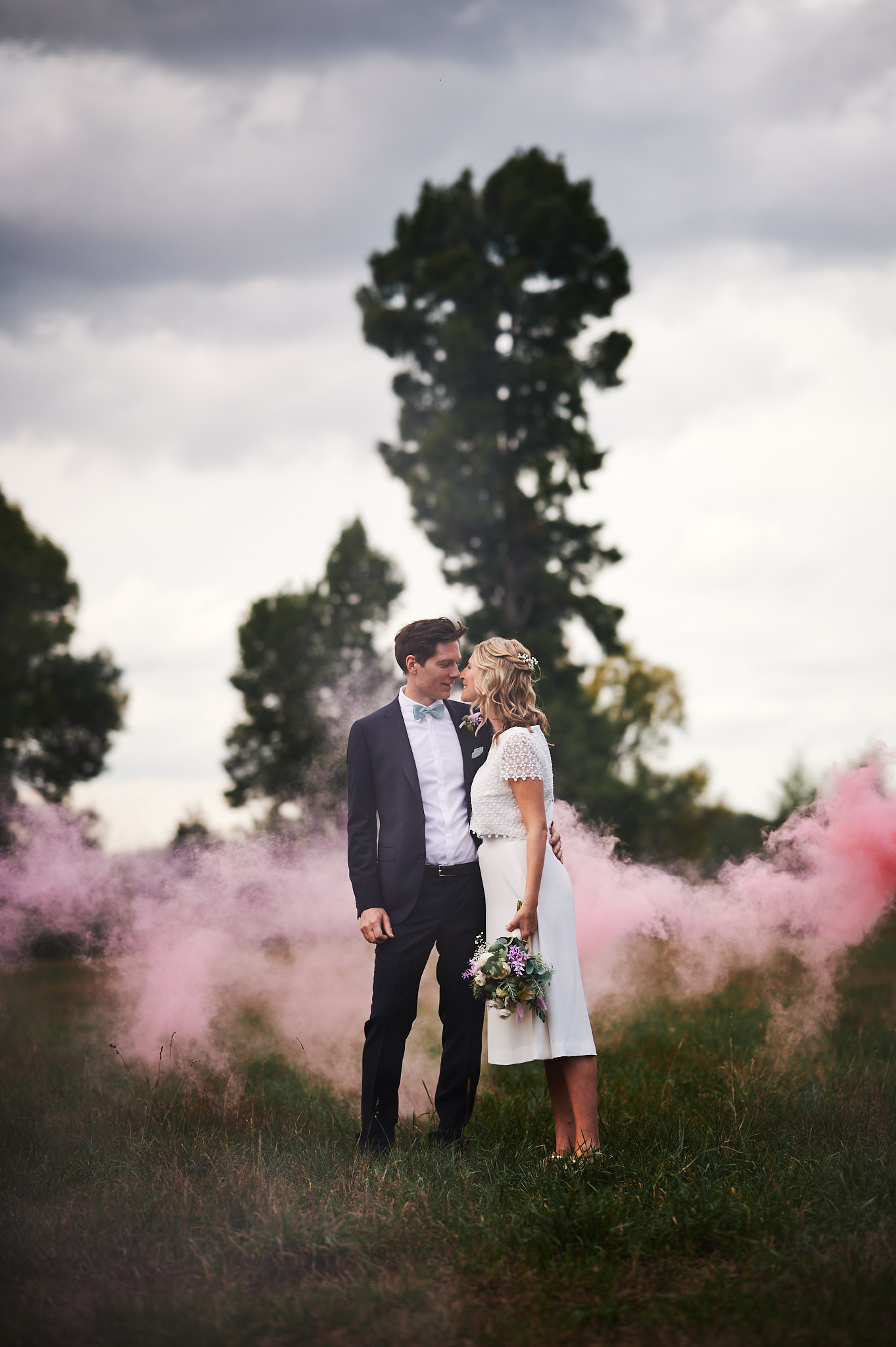 Ein sich umarmendes Paar auf einem Feld mit Schloss Wissen im Hintergrund und rosafarbenem Rauch.