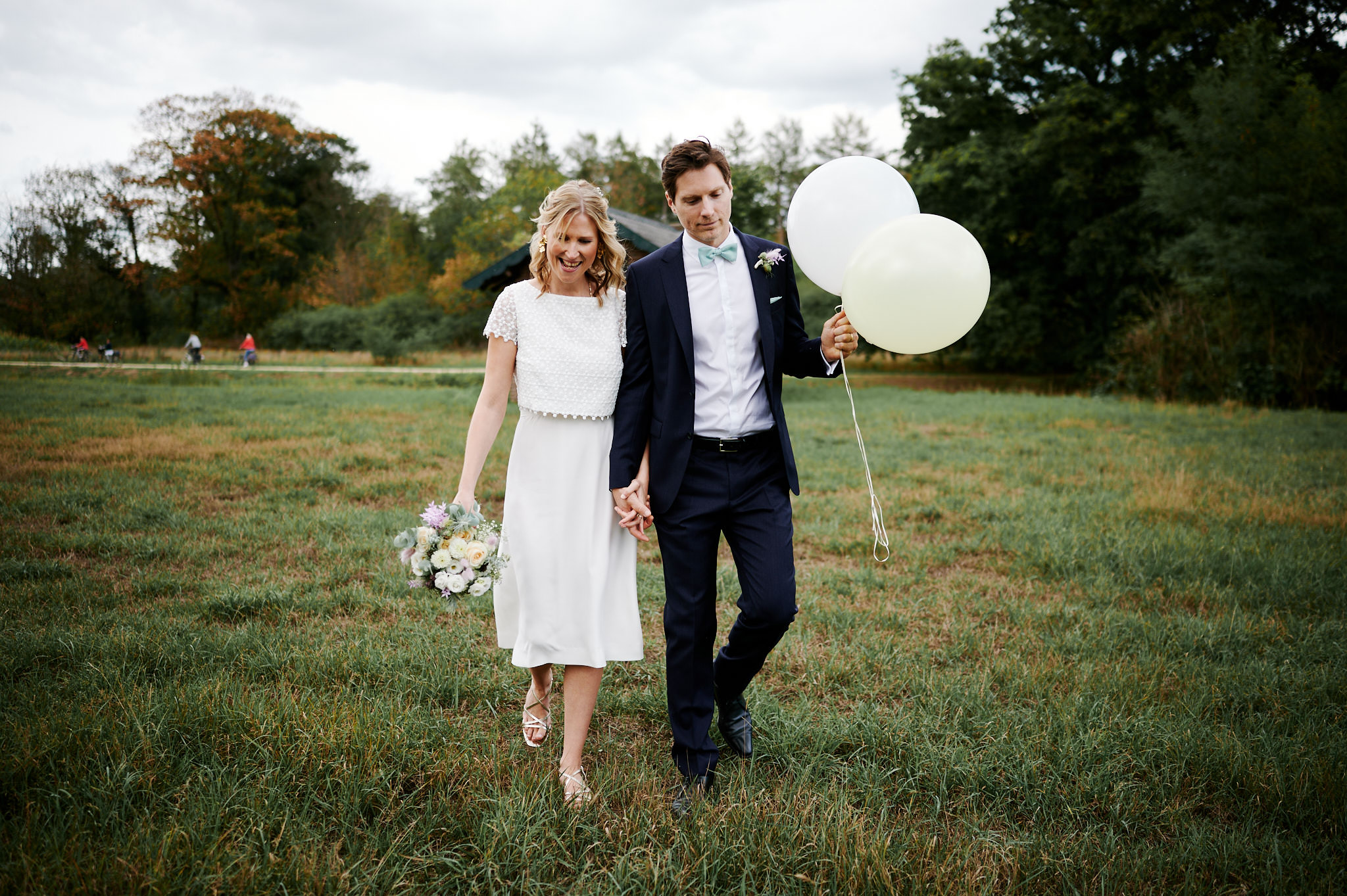 Braut und Bräutigam laufen durch ein Feld mit Luftballons auf Schloss Wissen.