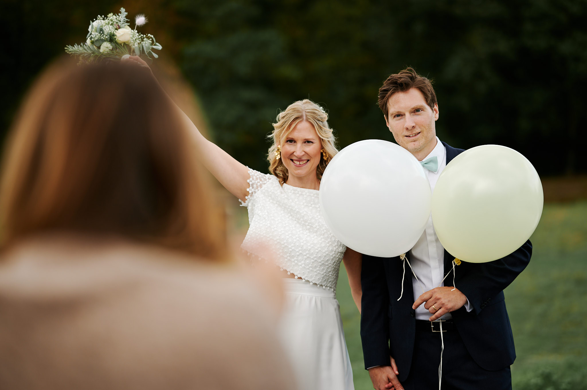 Braut und Bräutigam halten Luftballons in der Hand und werden von einem Gast bei einer Trauung im Freien auf Schloss Wissen fotografiert.