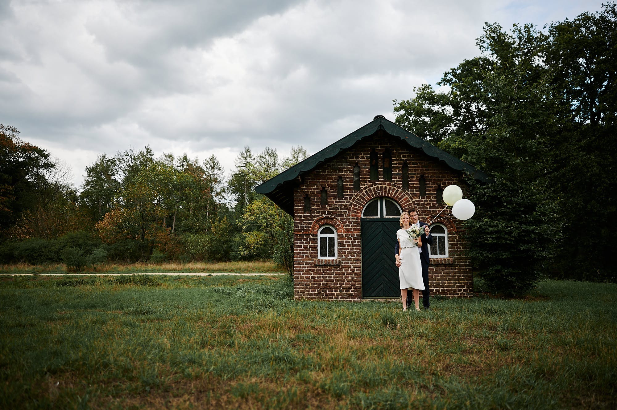 Eine Person steht neben einem kleinen Backsteingebäude mit Luftballons in ländlicher Umgebung und bietet eine idyllische Startseite.
