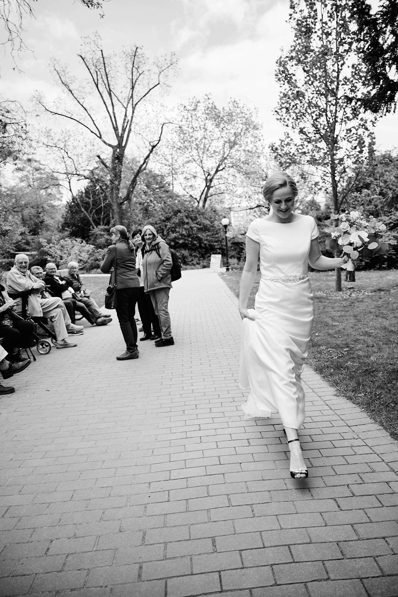 Eine Braut geht mit Schaulustigen im Hintergrund einen Parkweg entlang und schafft wunderschöne Hochzeitsbilder.