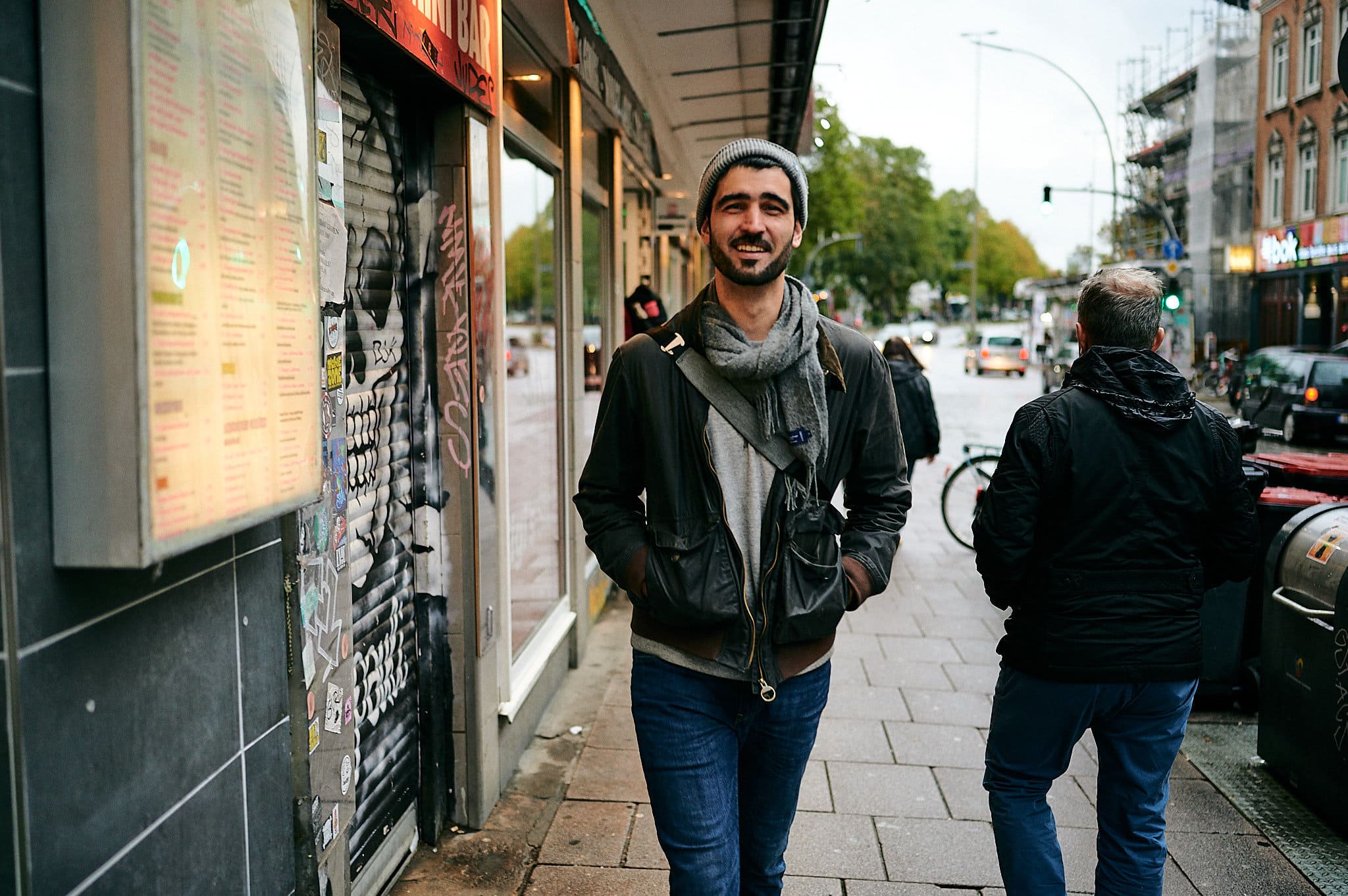 Mann lächelt, während er auf einem belebten Bürgersteig in der Stadt in der Nähe eines einladenden Ladens steht.