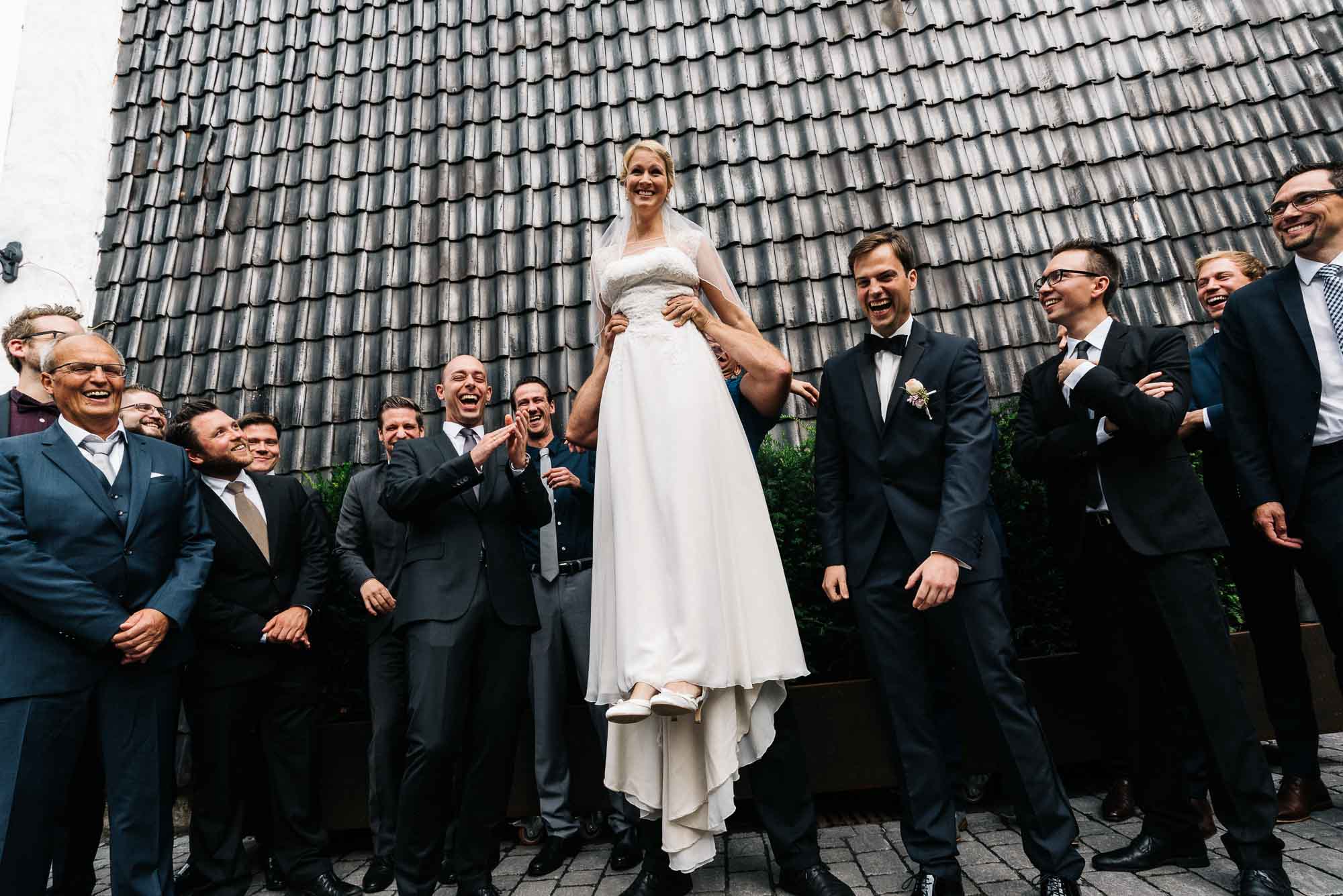 Braut wird bei einer Hochzeitsfeier über eine fröhliche Männergruppe gehoben, um unvergessliche Hochzeitsbilder zu machen.