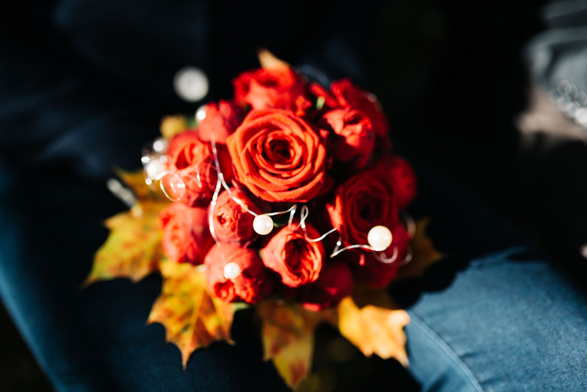 Ein Strauß roter Rosen mit eingestreuten Perlen und Herbstblättern, die im Sonnenlicht ruhen, perfekt für Hochzeitsbilder.