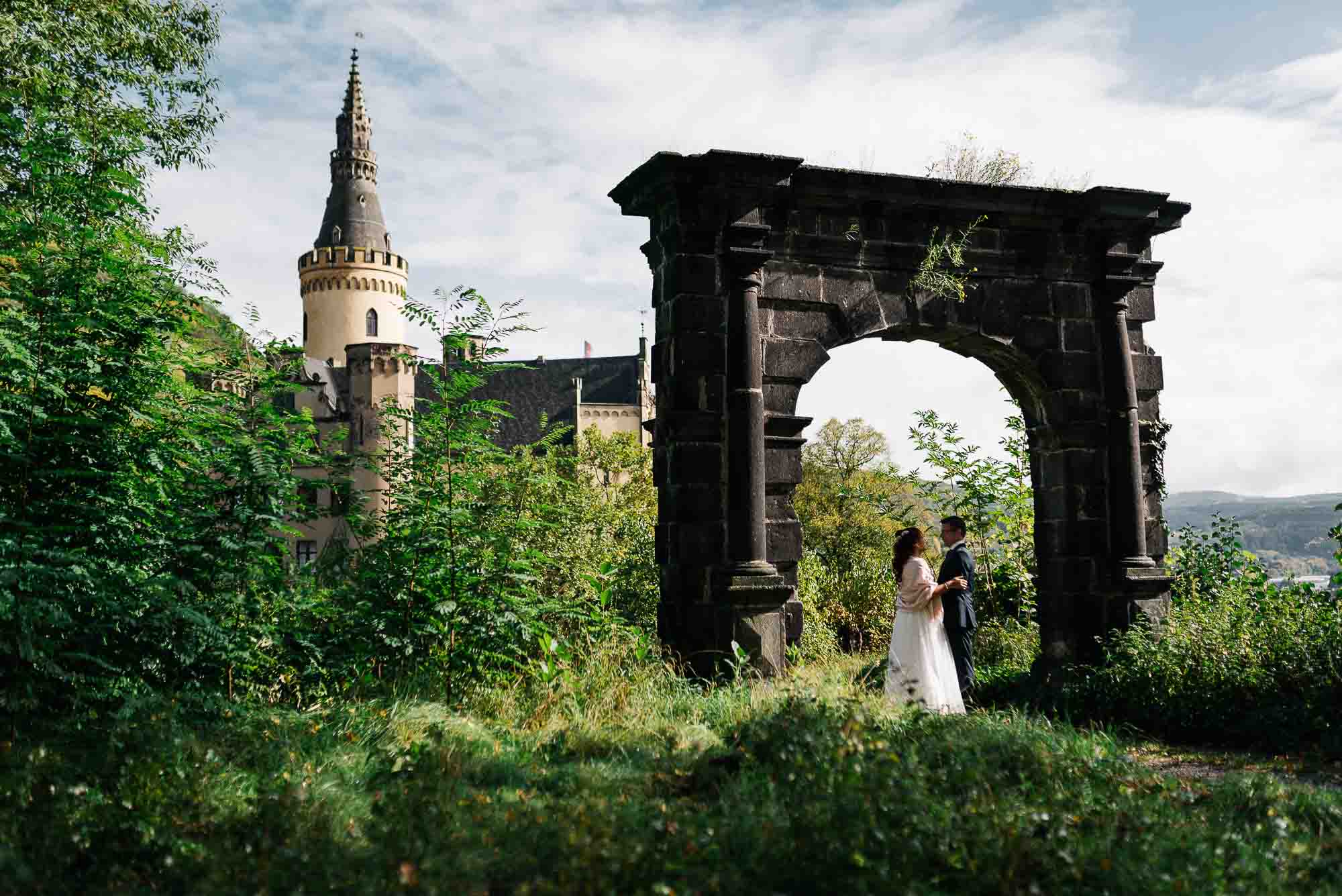 Ein Paar tauscht einen romantischen Moment unter einem Torbogen mit einem Burgturm im Hintergrund aus und fängt seine Hochzeitsbilder ein.