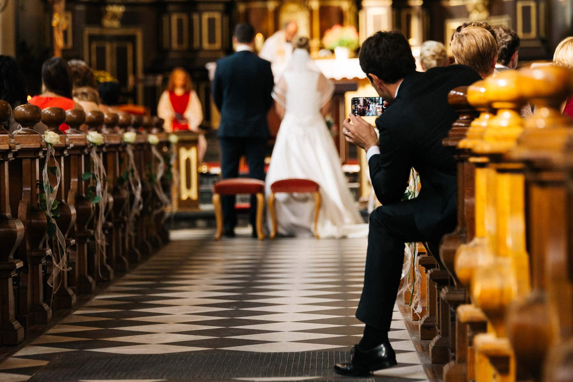 Eine laufende Hochzeitszeremonie mit einem Gast, der am Altar Hochzeitsfotos der Braut und des Bräutigams macht.